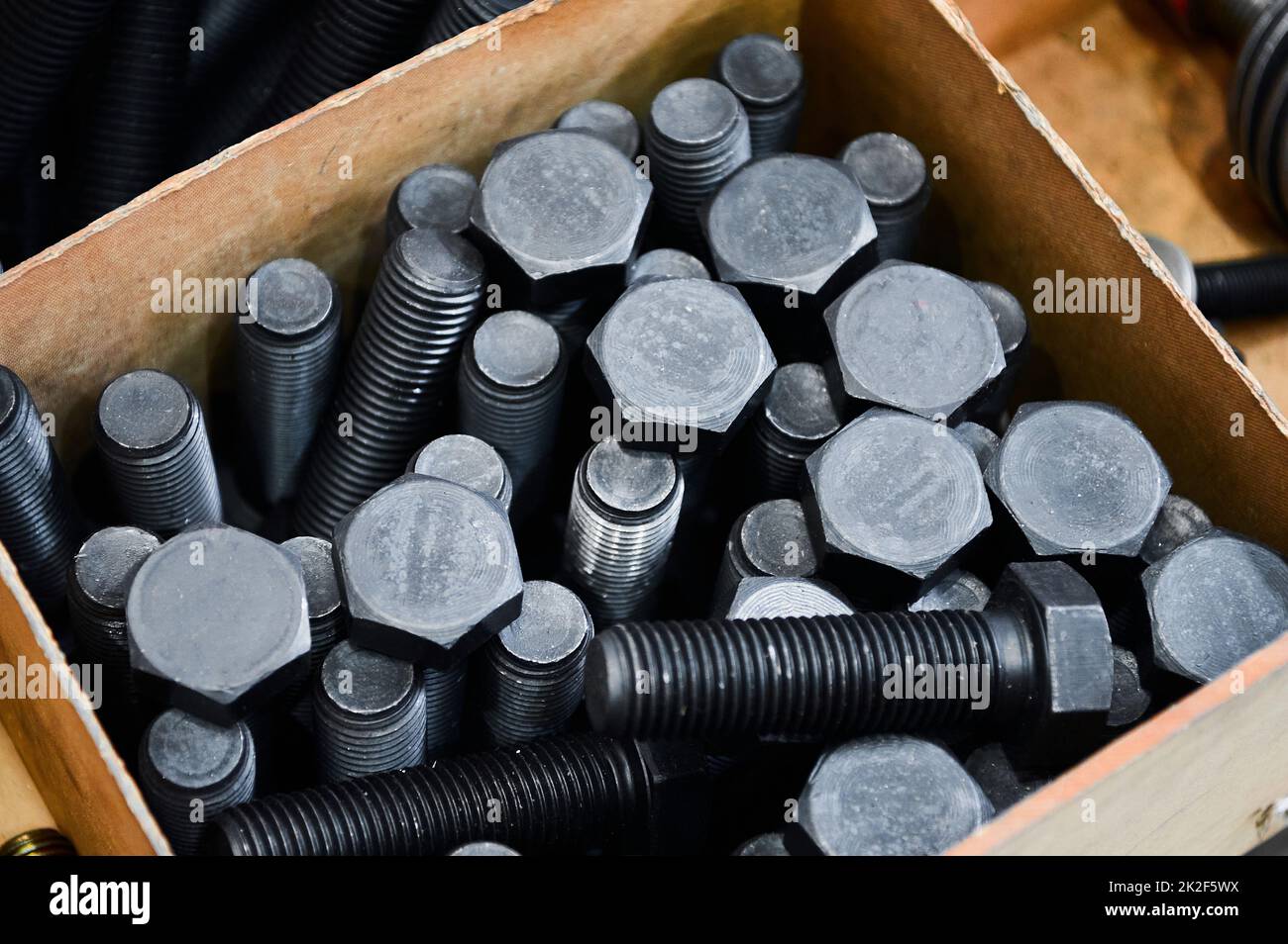 Pile of hardened blued metal bolts for fastening in crate Stock Photo