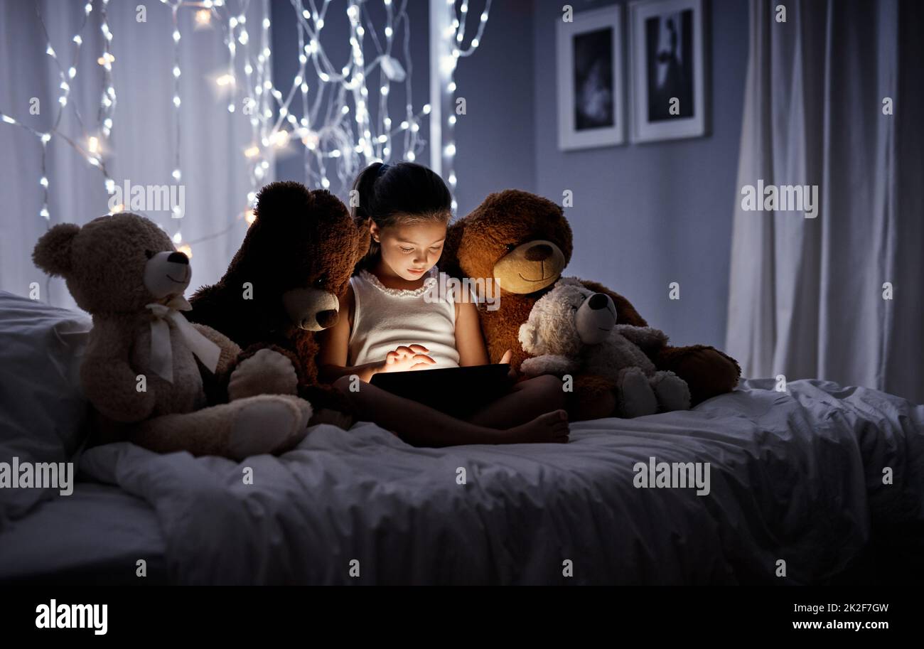 Introducing her teddies to technology. Shot of an adorable little girl using a digital tablet in bed at night. Stock Photo