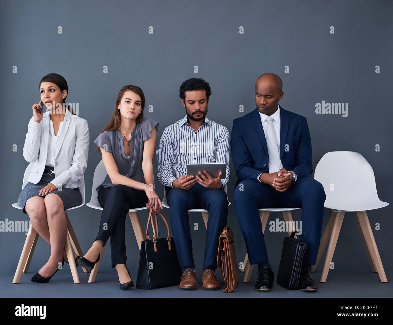 Trying to stay occupied while we wait. Studio shot of a group of corporate businesspeople waiting in line against a gray background. Stock Photo