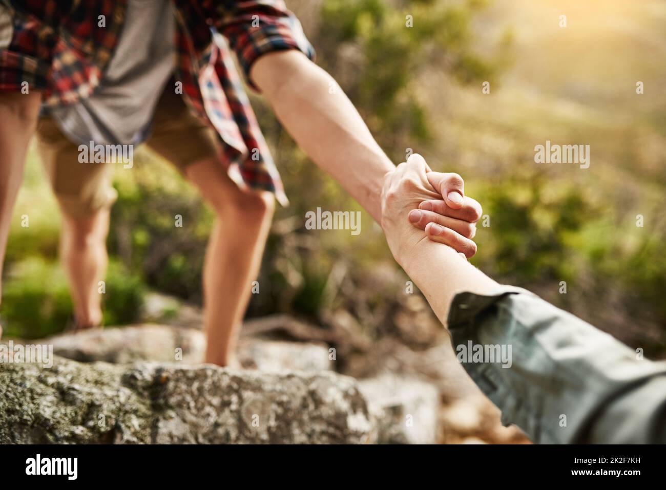 Alone we climb rocks, together we climb mountains. Cropped shot of hikers helping each other climb up a rock in nature. Stock Photo