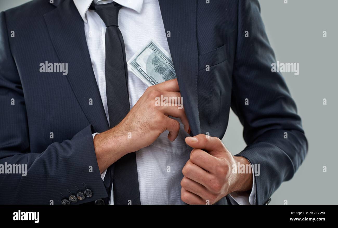 The real criminals wear suits, not balaclavas.... Cropped image of a businessman putting money in his pocket. Stock Photo