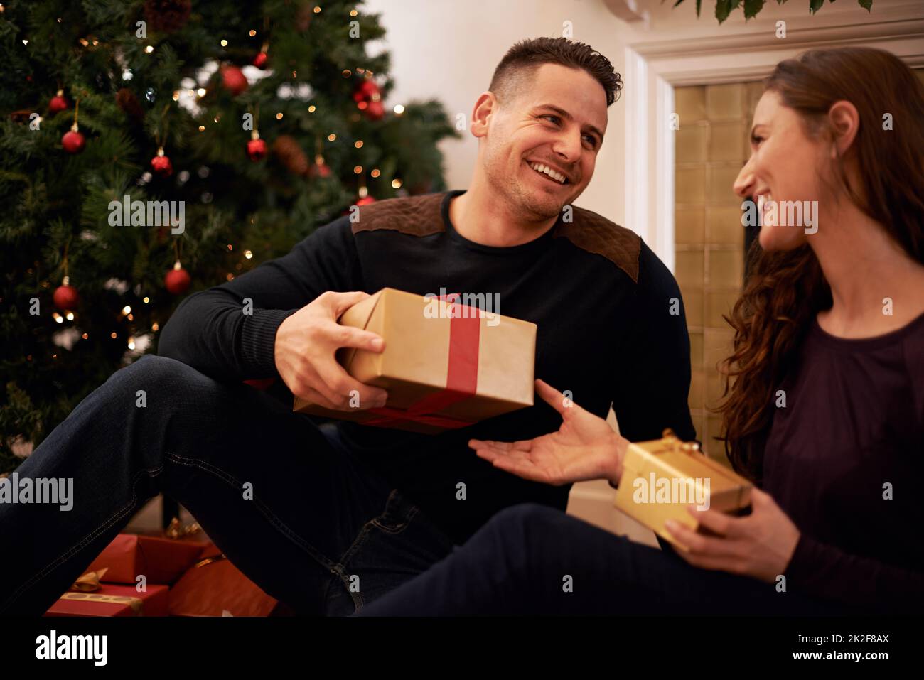 The best gift around the tree is love. A happy young couple opening presents on Christmas day. Stock Photo