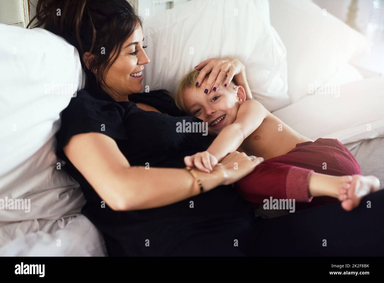 My precious little darling. Shot of a cheerful little boy and his mother hanging out on the bed at home while relaxing during the day. Stock Photo