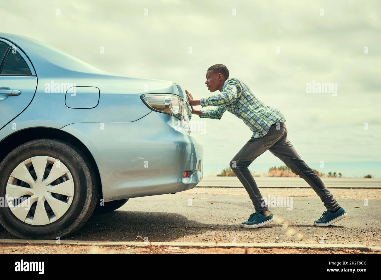 Sometimes youve gotta get out and push. Full length shot of a young man pushing his car along the road after breaking down. Stock Photo
