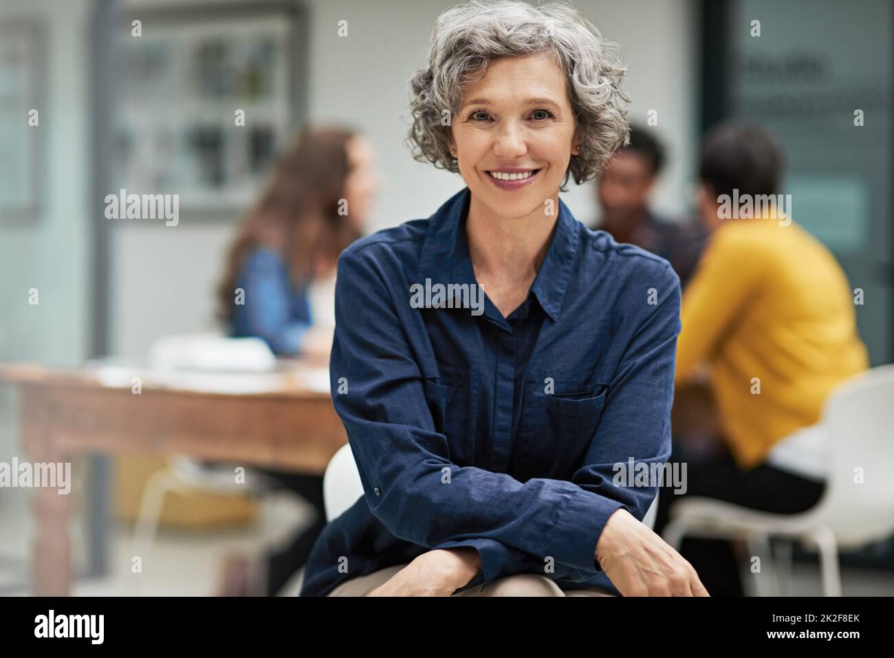 I turn challenges into opportunities. Portrait of a creative businesswoman sitting in the office while her colleagues work in the background. Stock Photo