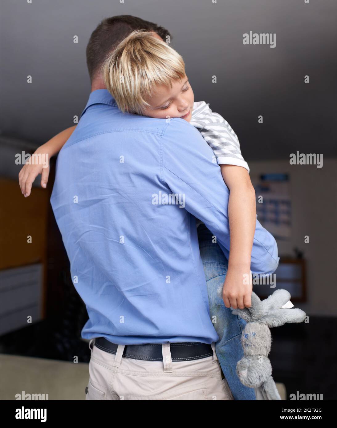 I wont go to bed without my teddy bear. A mature father coming home from work and hugging his exhausted little boy. Stock Photo