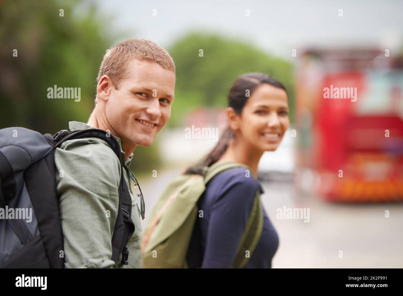 You dont need magic to dissapear, just a destination.... A travelling couple smile at the camera while waiting for their bus to arrive. Stock Photo
