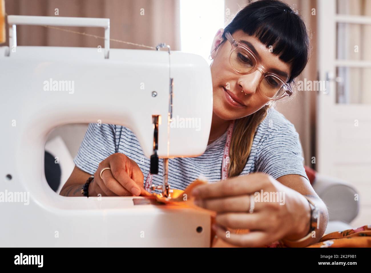 I just love seeing people in my beautiful creations. Cropped shot of a young woman stitching fabric using a sewing machine at home. Stock Photo