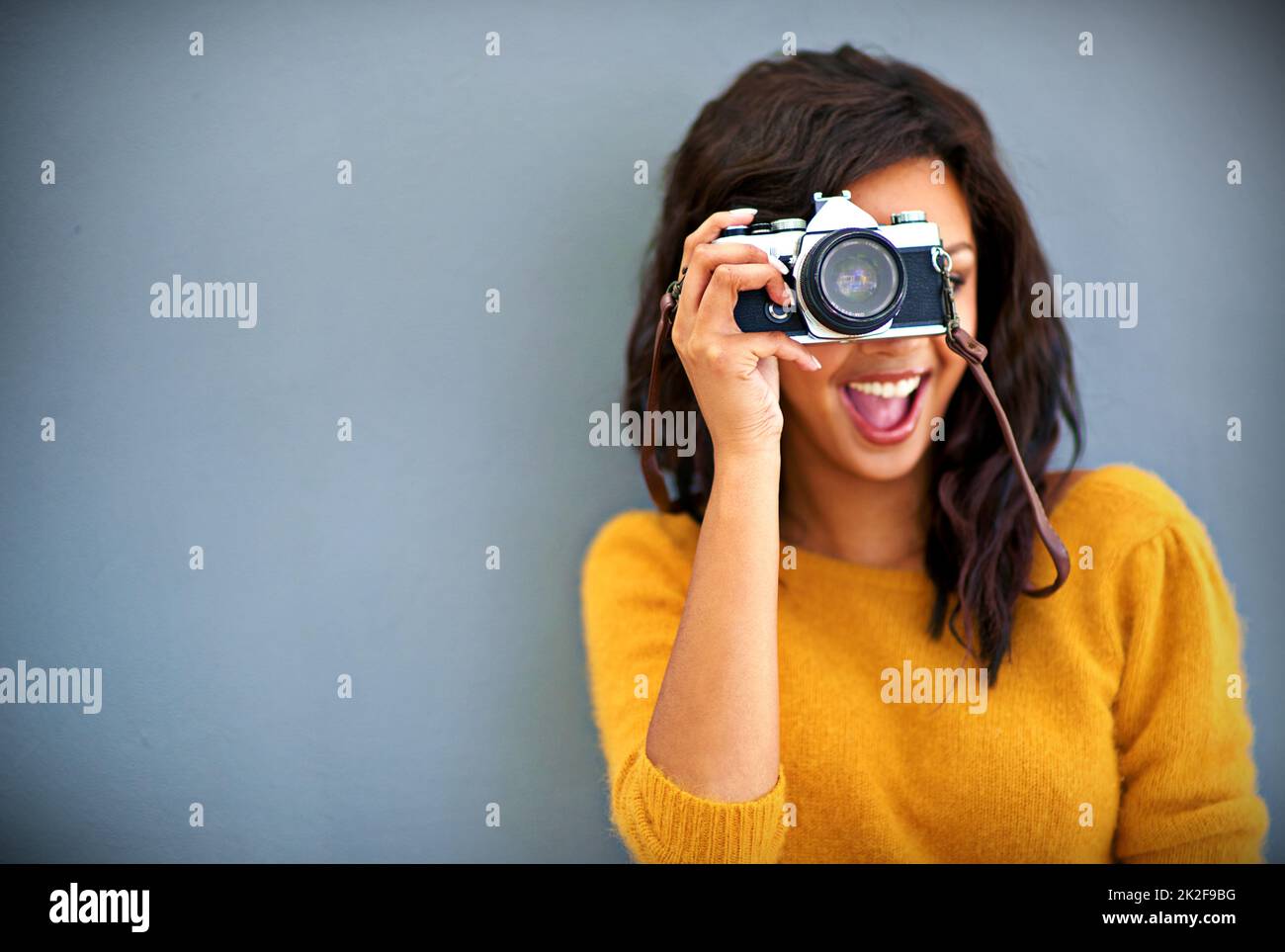 Happy snappy. Studio portrait of a young woman using a vintage camera against a gray background. Stock Photo