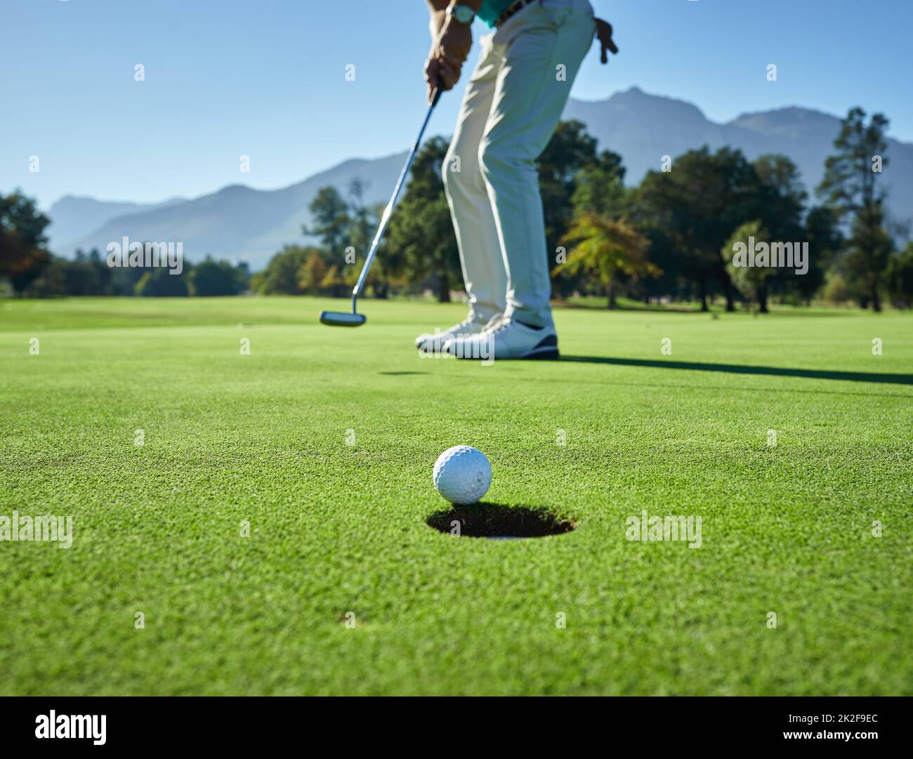 This is going to be in. Low angle shot of a unrecognizable man hitting a golfball into a hole on a golf course. Stock Photo