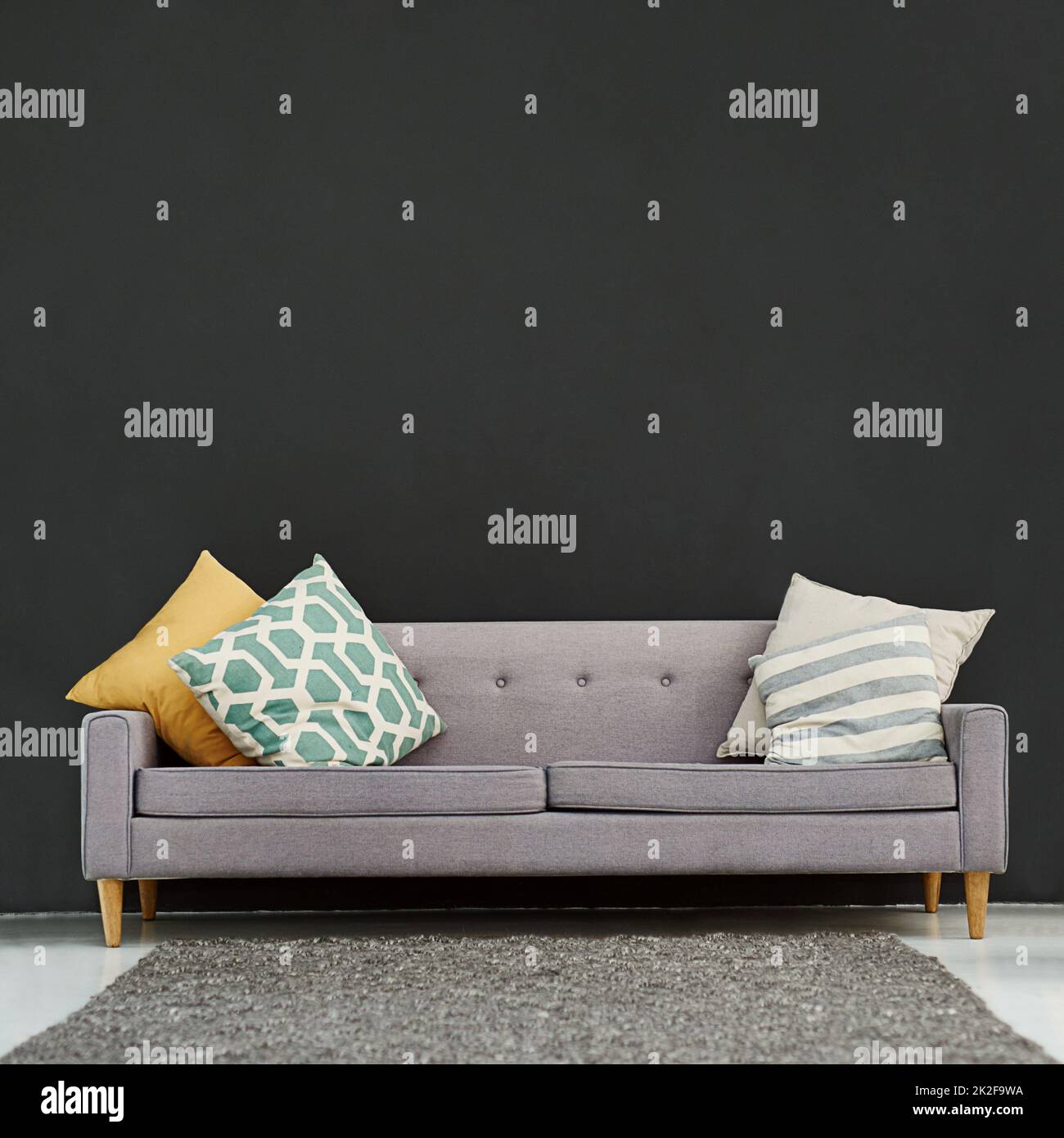 Functional and stylish for your office or home. Shot of a gray sofa with cushions against a black background. Stock Photo