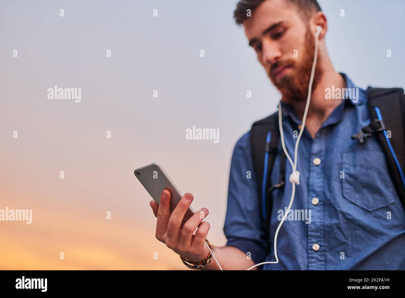 Everything he needs is right in his hand. Low angle shot of a handsome young man listening to music on his cellphone while walking through the city. Stock Photo