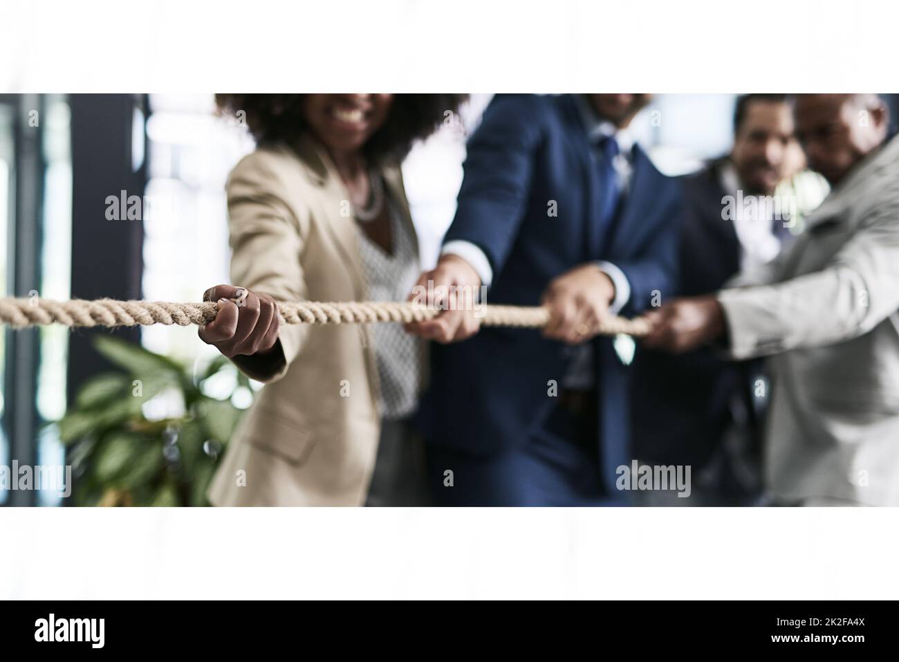Challenges can be overturned with teamwork. Closeup shot of a group of unrecognizable businesspeople pulling together on a rope in an office. Stock Photo