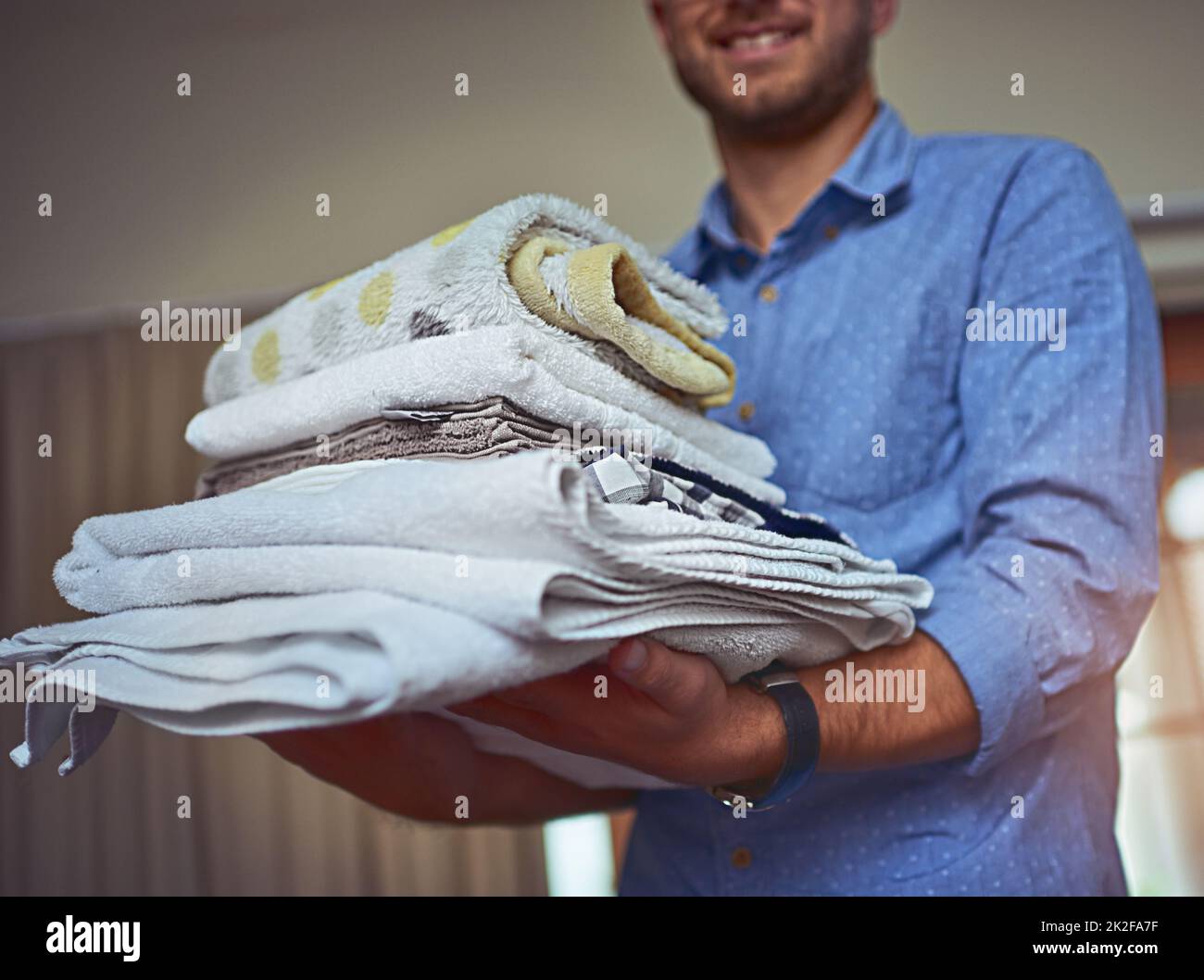 Anyone call for clean towels. Cropped shot of a young man holding a load of freshly folded clean laundry. Stock Photo