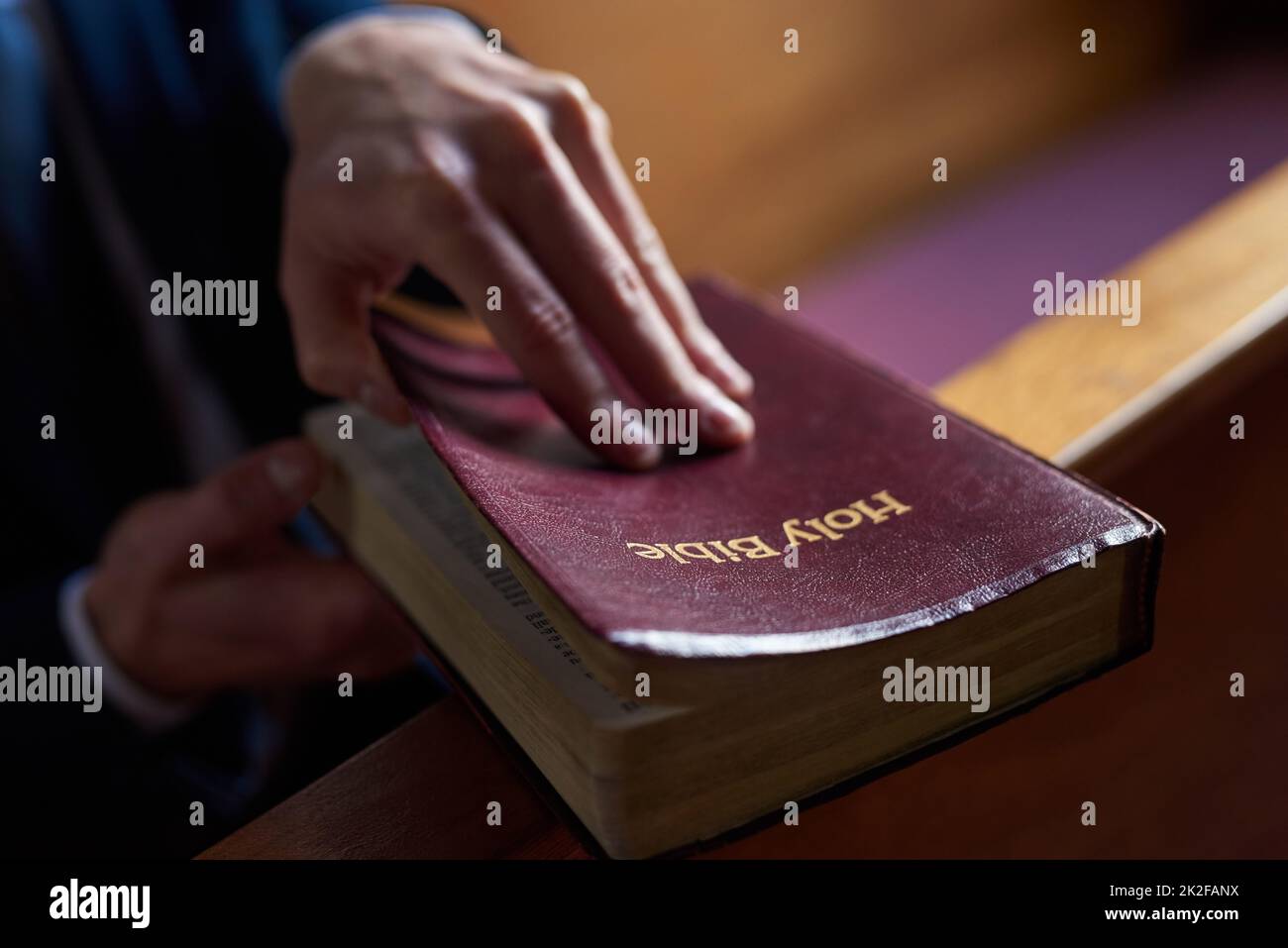 Finding comfort in the good book. Cropped shot of a man opening a bible while sitting in a pew at church. Stock Photo