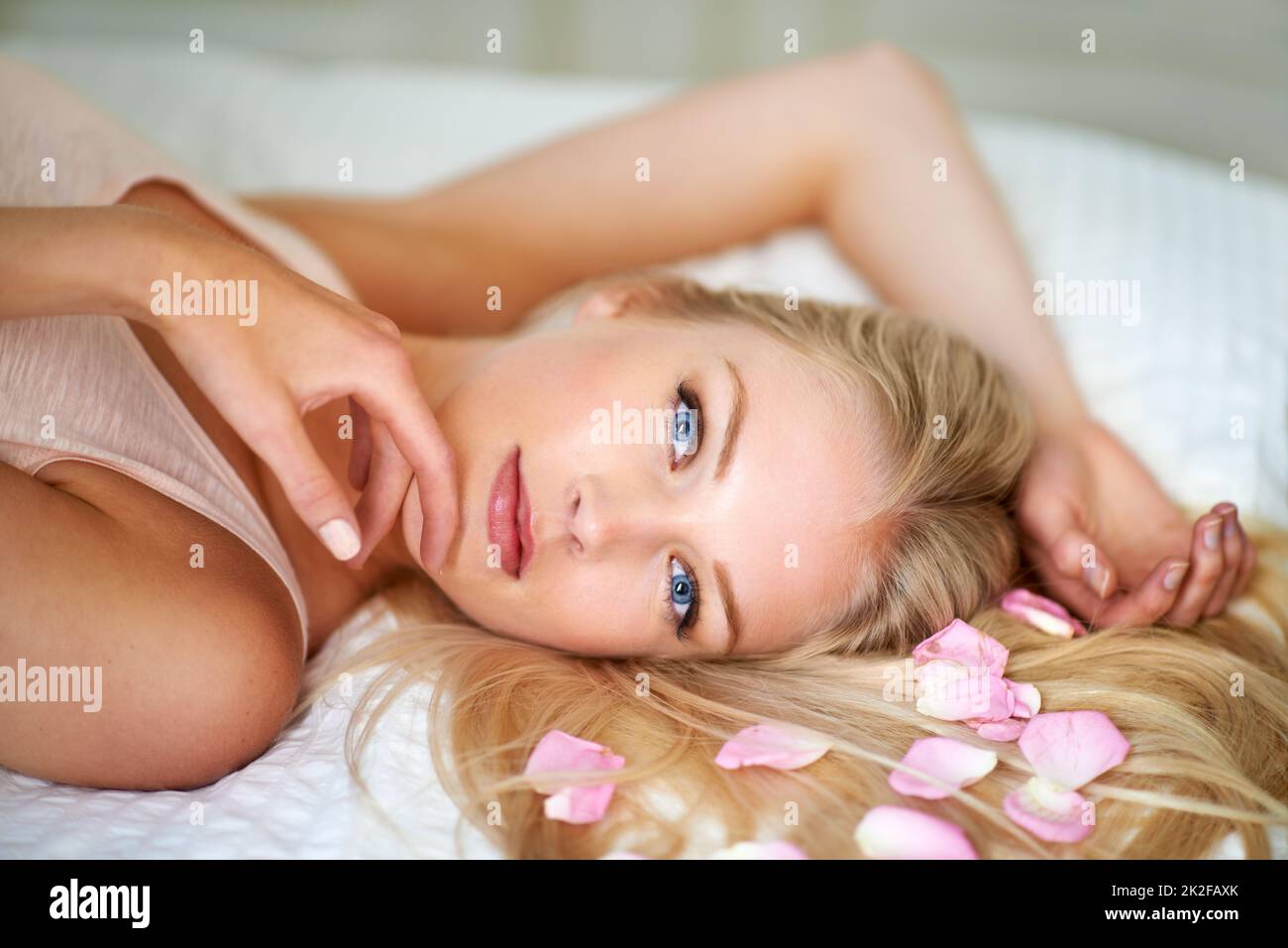 Pretty as a flower. Portrait of an attractive woman lying on her bed with rose petals in her hair. Stock Photo