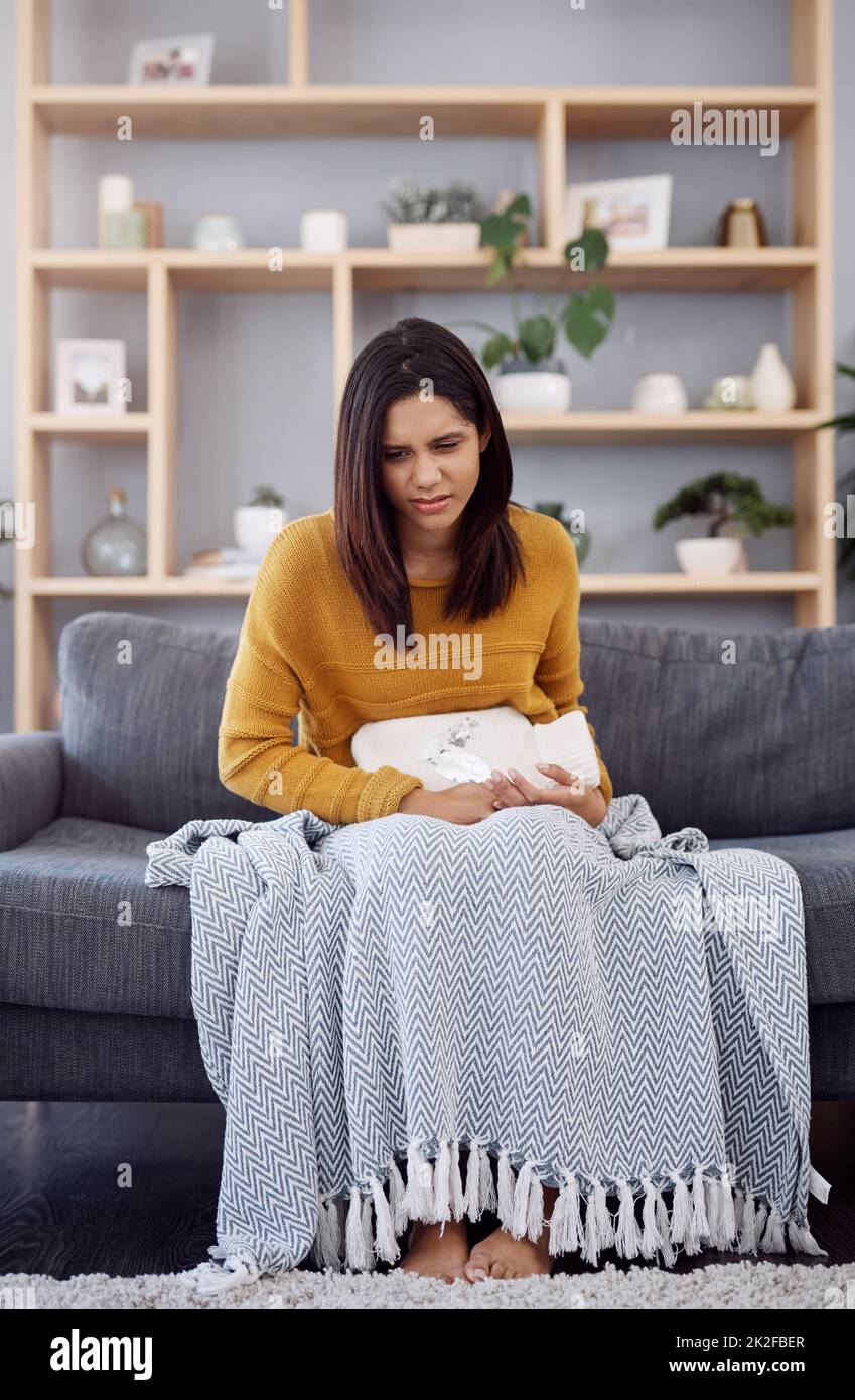 This pain is unbearable. Full length shot of an attractive young woman suffering from stomach cramps while sitting on a sofa at home. Stock Photo