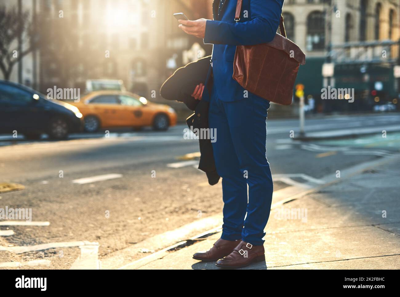 On the busy streets of the city. Low angle shot of a unrecognizable man texting on his phone while waiting for a taxi to take him to work in the morning. Stock Photo