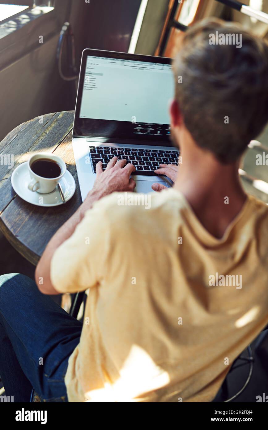 Doing some business at the bistro. Shot of a young man using a laptop in a cafe. Stock Photo