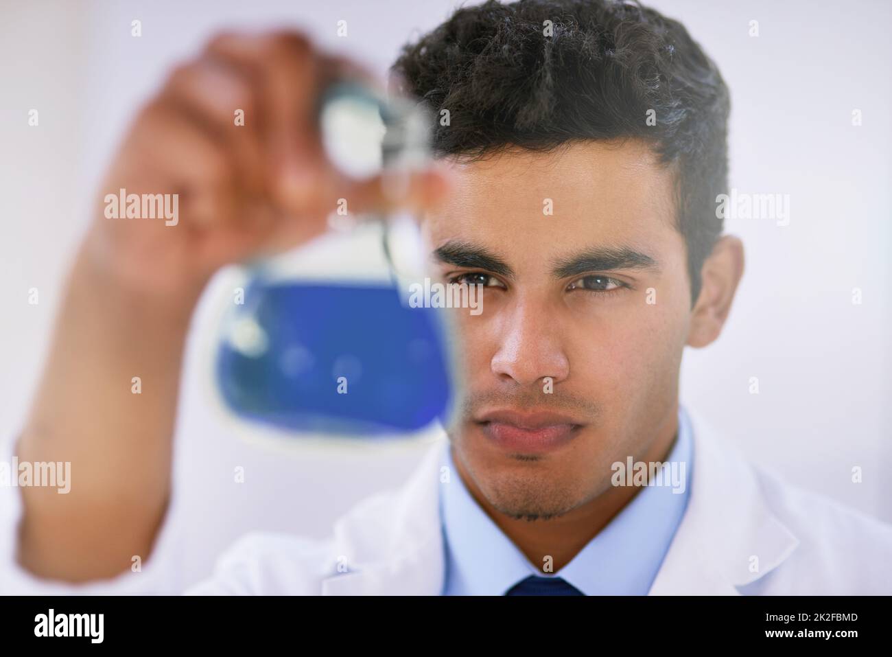 Scrutinizing samples. Shot of a lab technician examining a beaker of blue liquid while standing in a lab. Stock Photo
