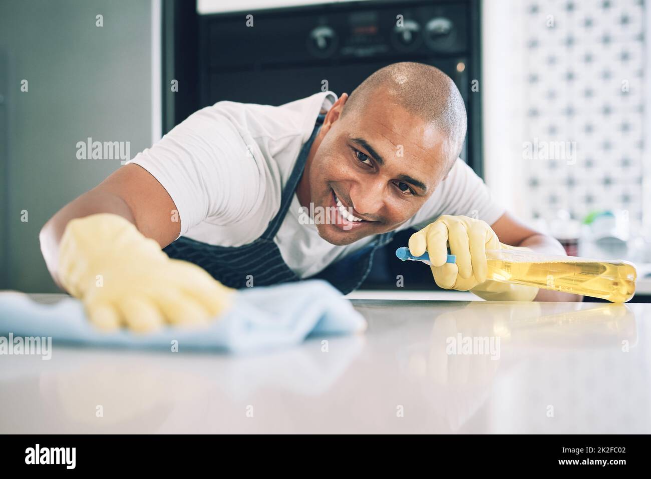 This counter needs to be squeaky clean. Shot of a young man wiping a surface at home. Stock Photo