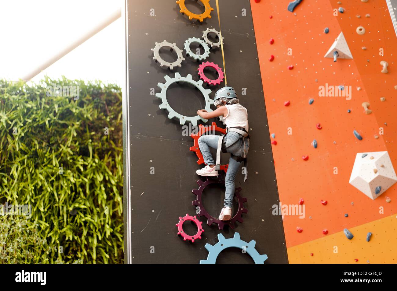 Child climbing on wall in amusement centre. Climbing training for children. Little girl in dressed climbing gear climb high. Extreme active leisure for kids. Caucasian little girl 5 years old. Stock Photo