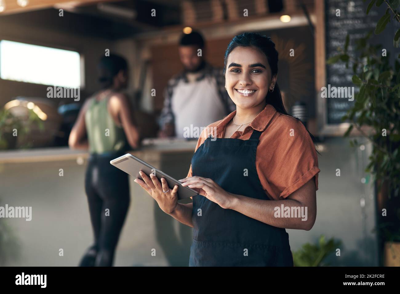 Lets get you seated. Shot of an attractive young woman standing outside her restaurant and using a digital tablet. Stock Photo