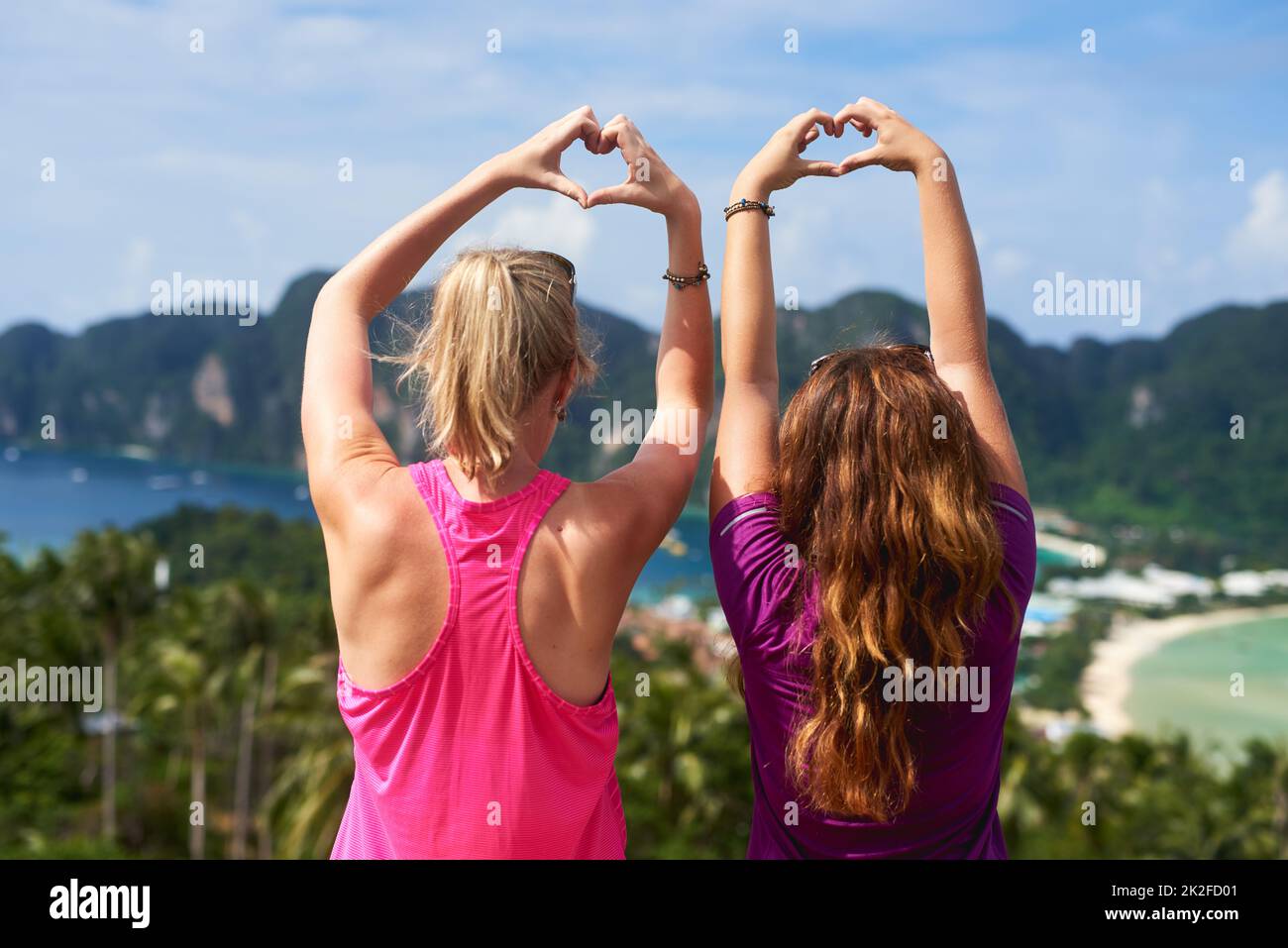Live for the moments that make life beautiful. Rear view shot of two young woman making a heart gesture while facing a scenic landscape. Stock Photo