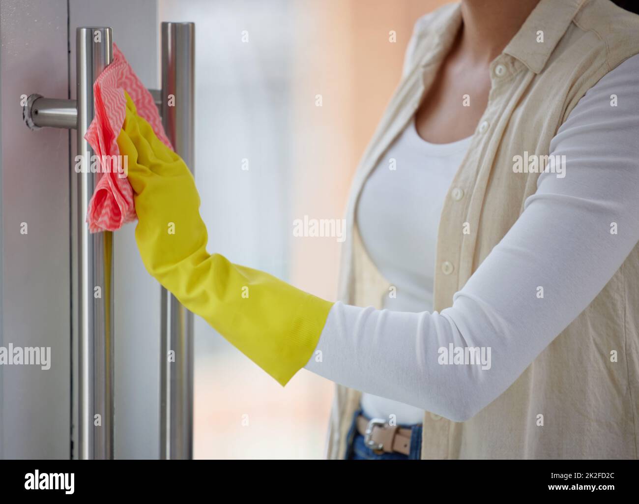 Everything your hands touch should be clean. Shot of a woman cleaning the handles of her door. Stock Photo