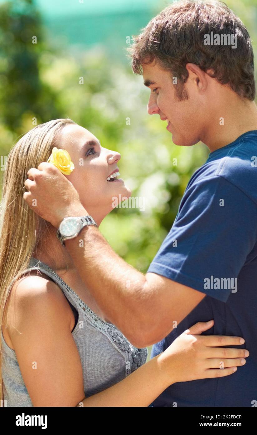 Shes my precious flower. A young man placing a flower over his girlfriends ear while looking lovingly at her. Stock Photo