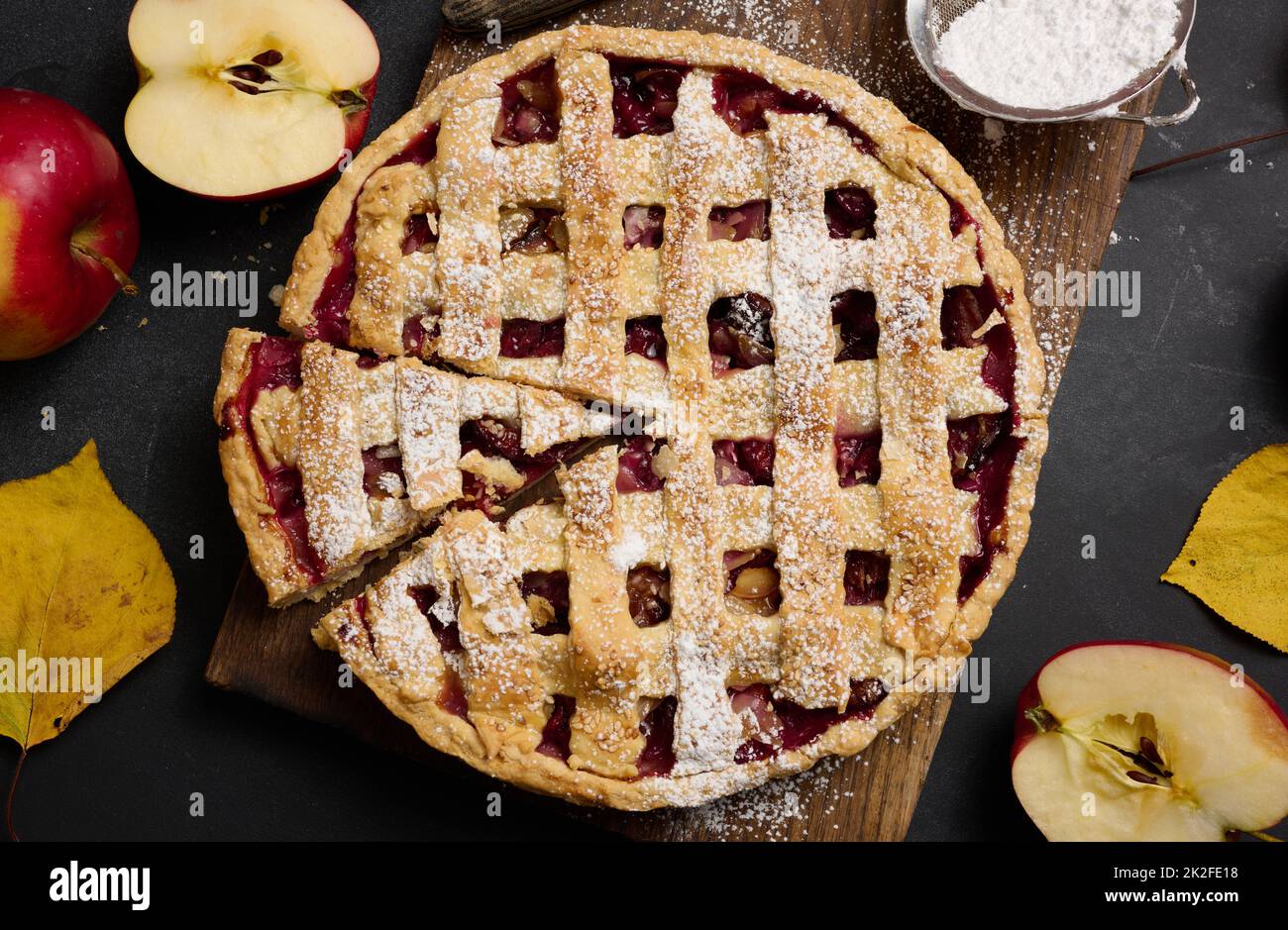 baked round traditional apple pie on brown wooden board and fresh red apples, top view Stock Photo