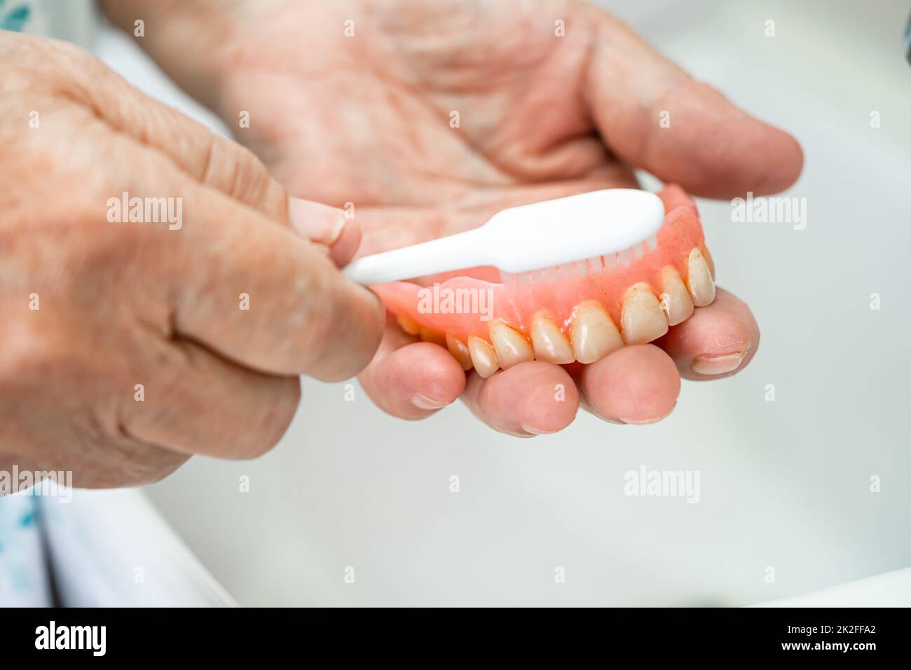 Asian senior or elderly old woman patient use toothbrush to clean partial denture of replacement teeth. Stock Photo