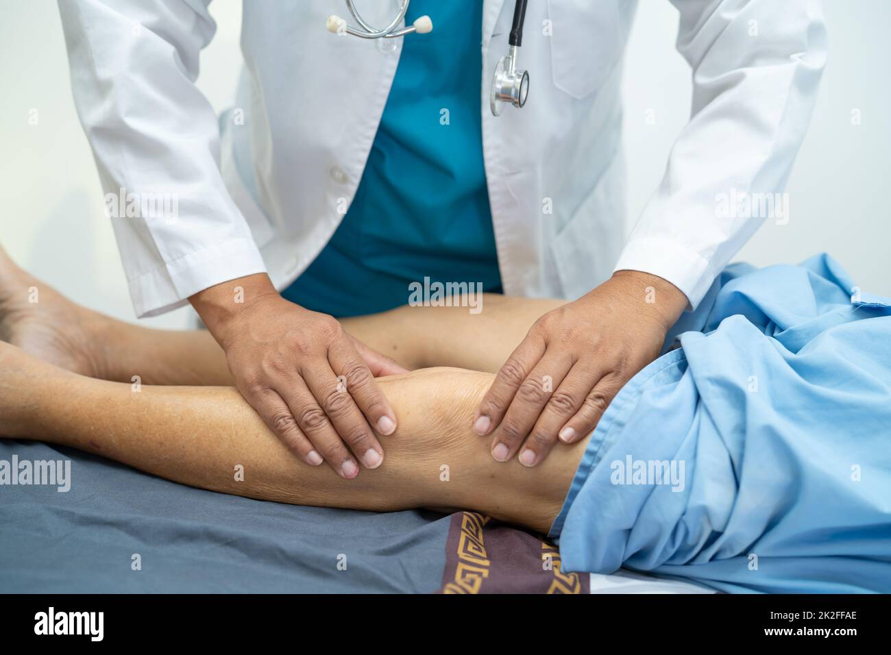 Asian doctor physiotherapist examining, massaging and treatment knee and leg of senior patient in orthopedist medical clinic nurse hospital. Stock Photo
