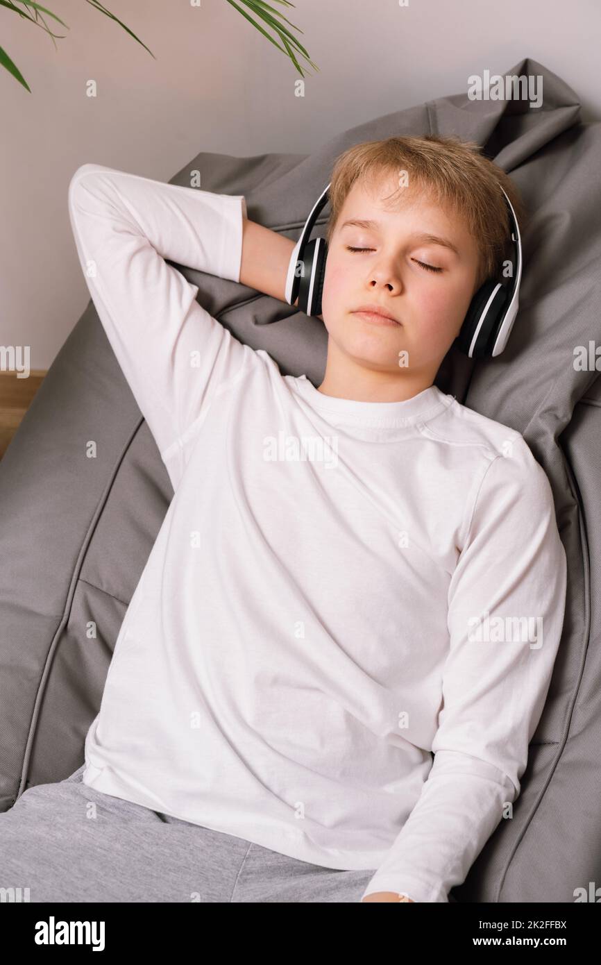 Relaxed teenager lies on a bean bag chair with headphones. White t