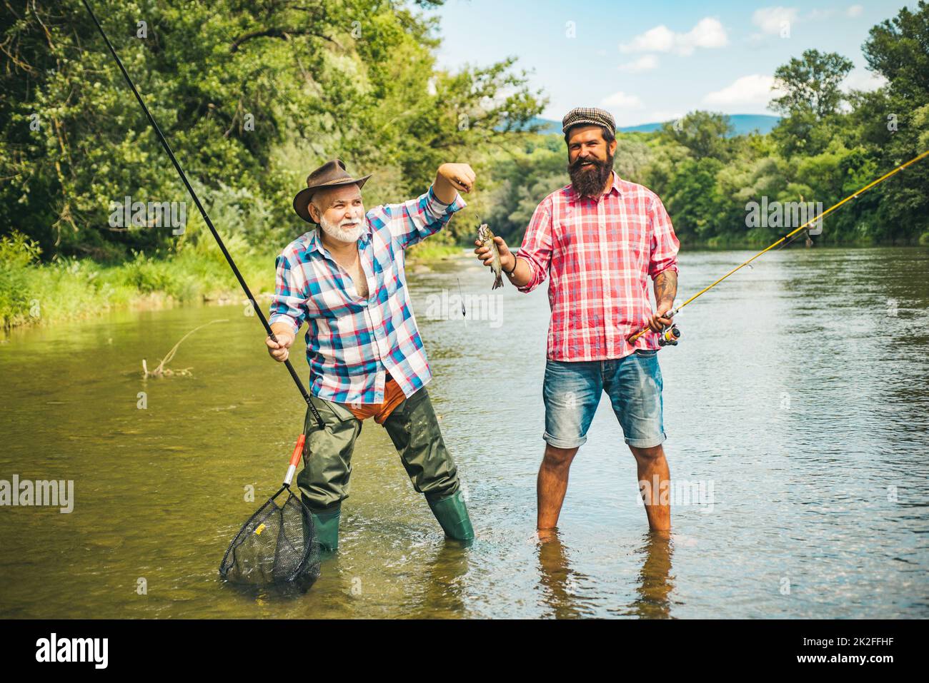 Man friends. Two men friends fishing. Flyfishing angler makes cast, standing in river water. Old and young fisherman. Stock Photo