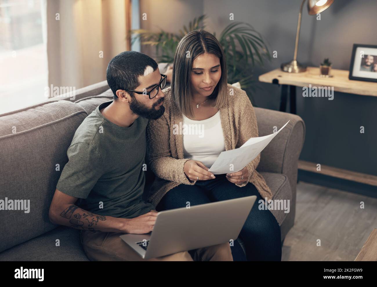 All hands on deck for creating a stable home. Shot of a young couple using a laptop while going through paperwork at home. Stock Photo
