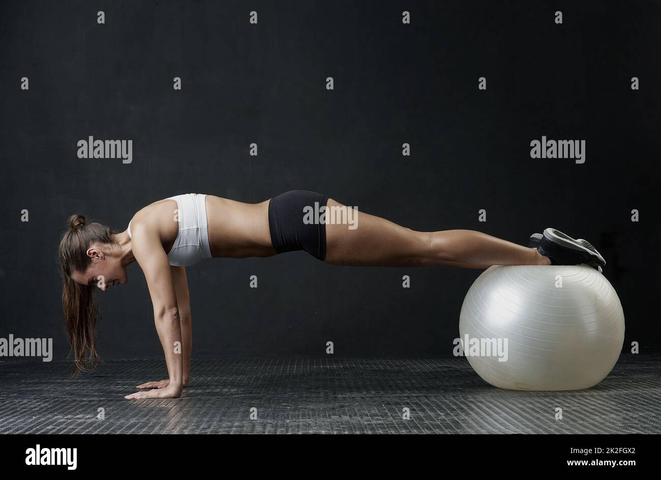 Get on her level. Studio shot of an attractive young woman working out against a dark background. Stock Photo