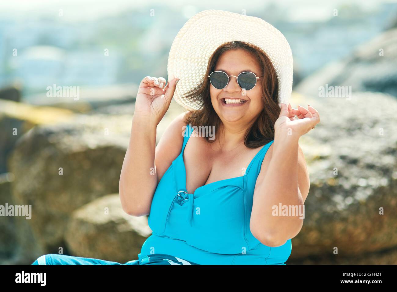 Confidence is wearing that one piece at any age. Shot of an attractive mature woman sitting alone during a day out on the beach. Stock Photo