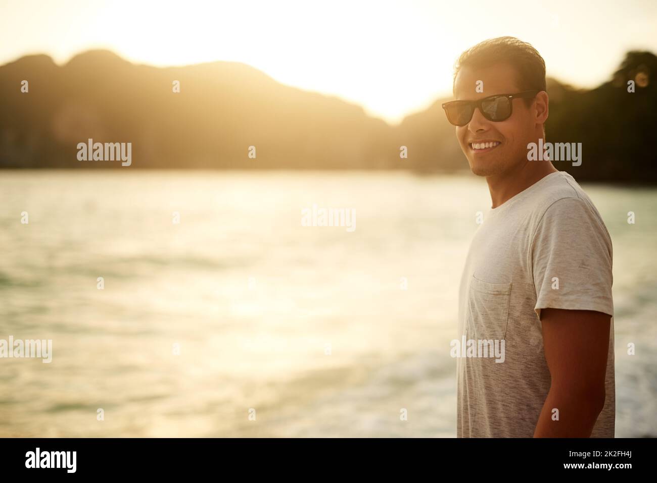 No better place than the beach. Portrait of a handsome young man standing on the beach at sunset. Stock Photo