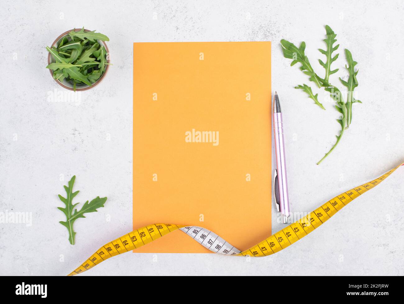 Planning a diet, arugula salad and tailor tape measure around the empty paper, healthy food and lifestyle, loosing weight Stock Photo