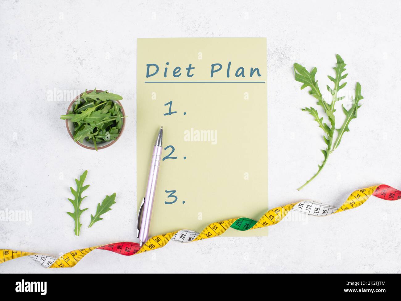 On the paper stands diet plan, arugula salad and tailor tape measure around the note, healthy food and lifestyle, loosing weight Stock Photo