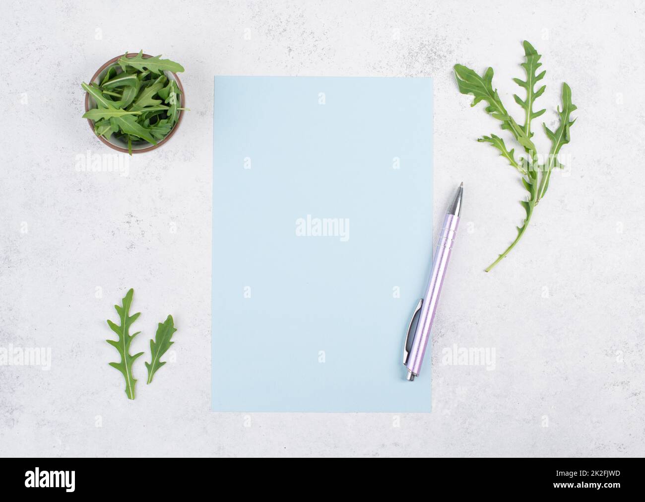 Blank colored paper with a pen, arugula salad leaves, copy space for text, recipe for cooking, preparing food, healthy lifestyle, diet Stock Photo