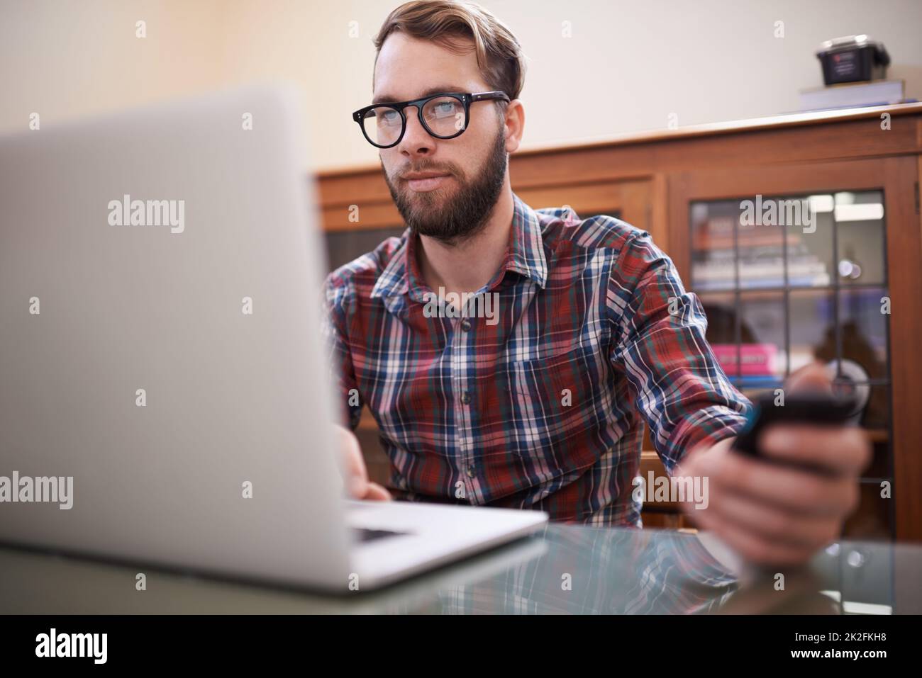 Using all the latest tech. a handsome young hipster working on a laptop. Stock Photo