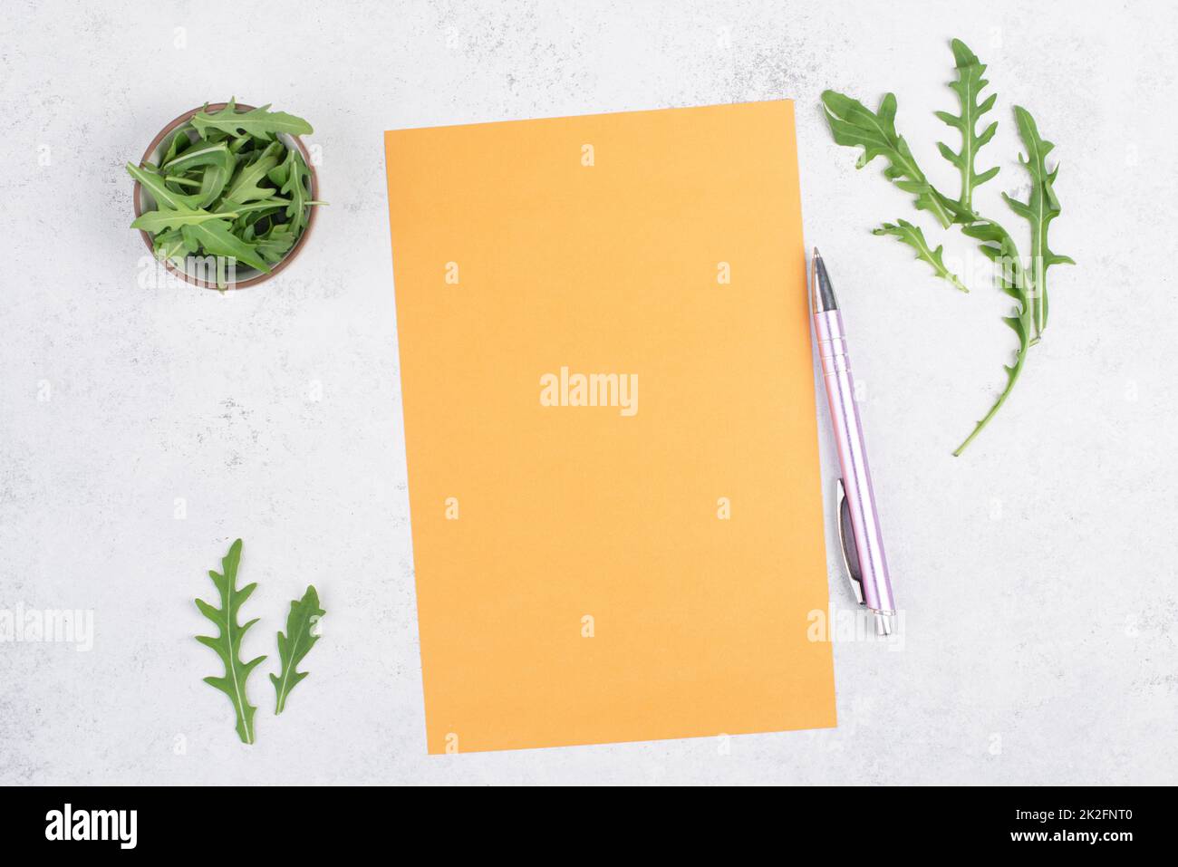 Blank colored paper with a pen, arugula salad leaves, copy space for text, recipe for cooking, preparing food, healthy lifestyle, diet Stock Photo