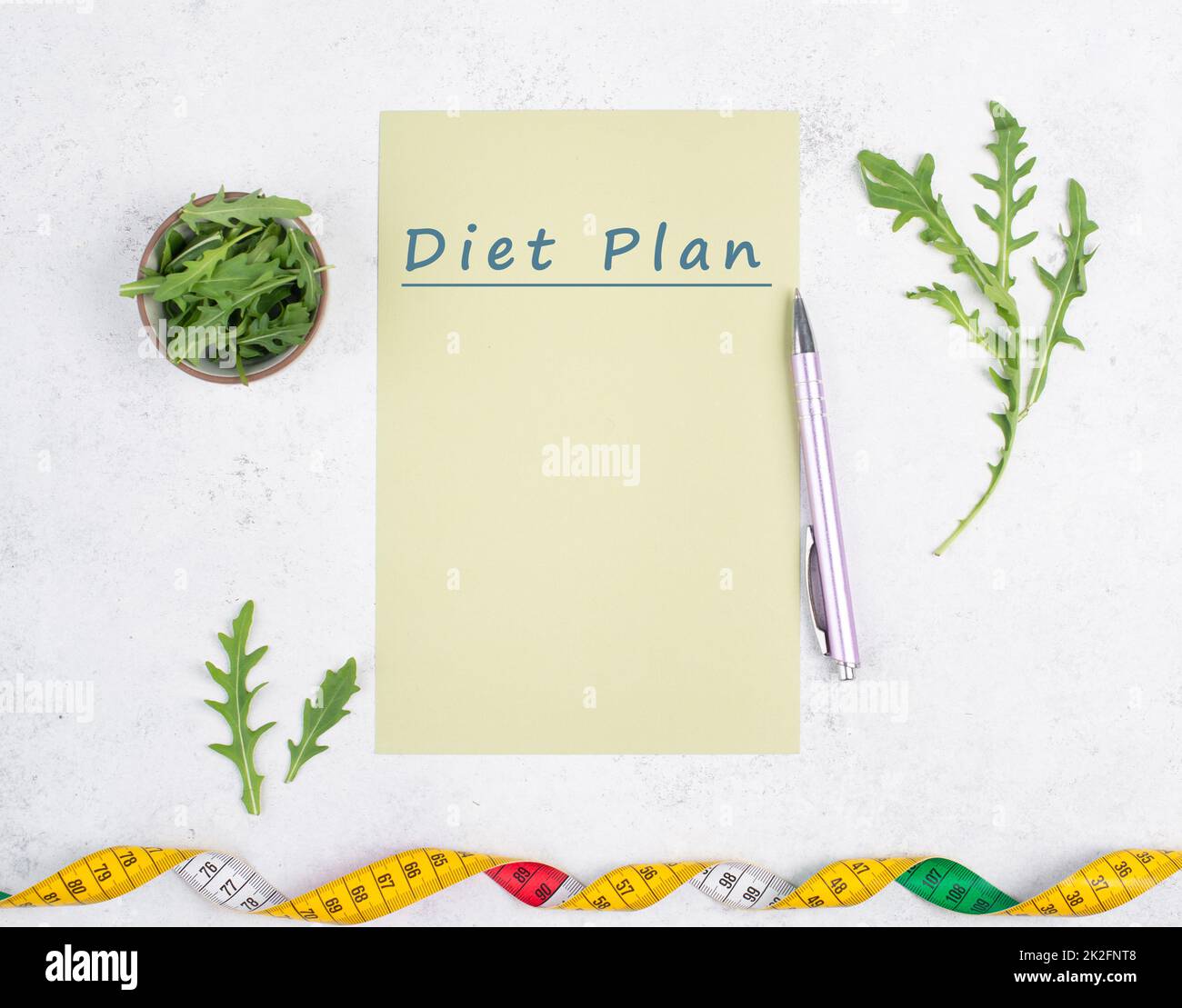 On the paper stands diet plan, arugula salad and tailor tape measure around the note, healthy food and lifestyle, loosing weight Stock Photo