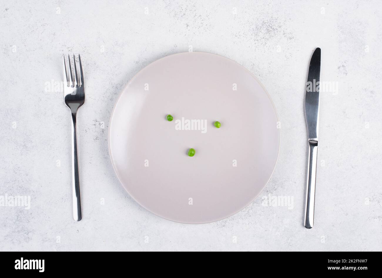 Three green peas on a plate, fork and knife on the table, diet and loosing weight concept, healthy lifestyle Stock Photo