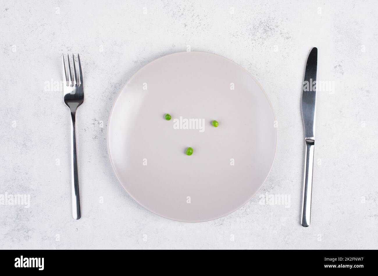 Three green peas on a plate, fork and knife on the table, diet and
