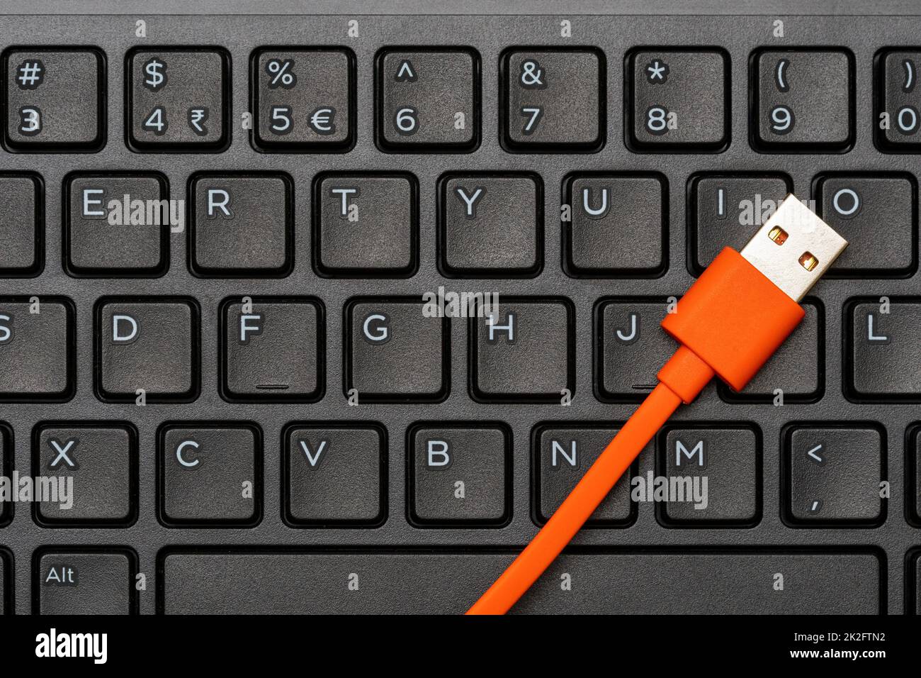 Computer keyboard and orange USB cable for data transfer Stock Photo