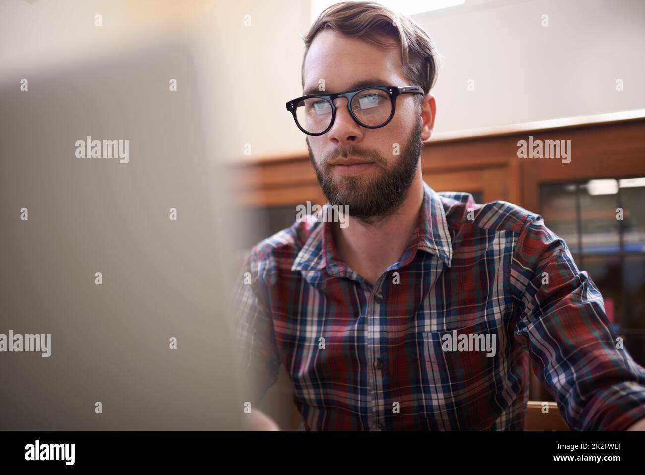 Using all the latest tech. a handsome young hipster working on a laptop. Stock Photo