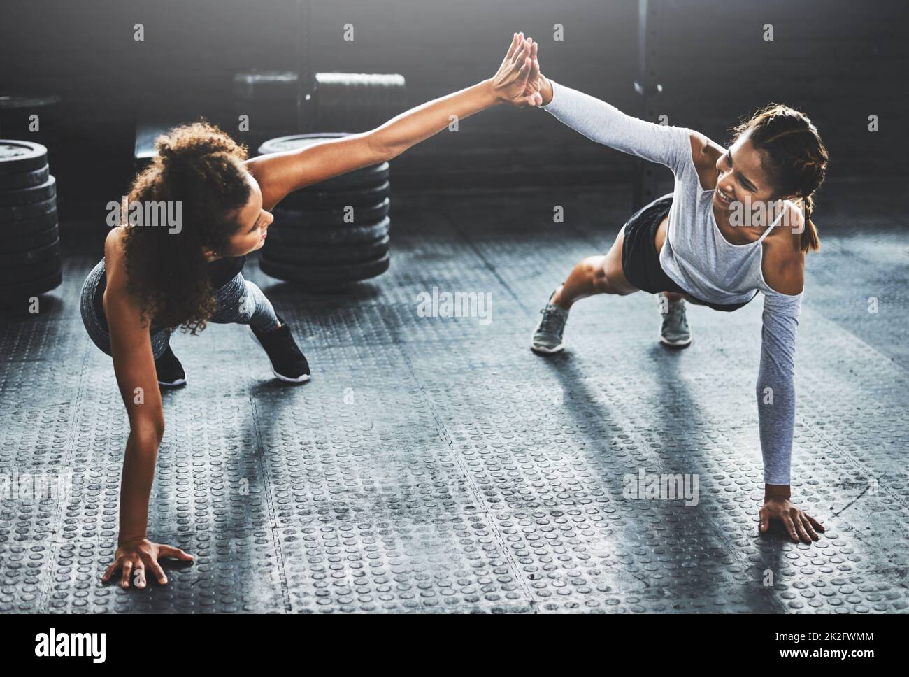 Bring your best friend and give it your best. Shot of two young women giving each other a high five while doing push ups at the gym. Stock Photo